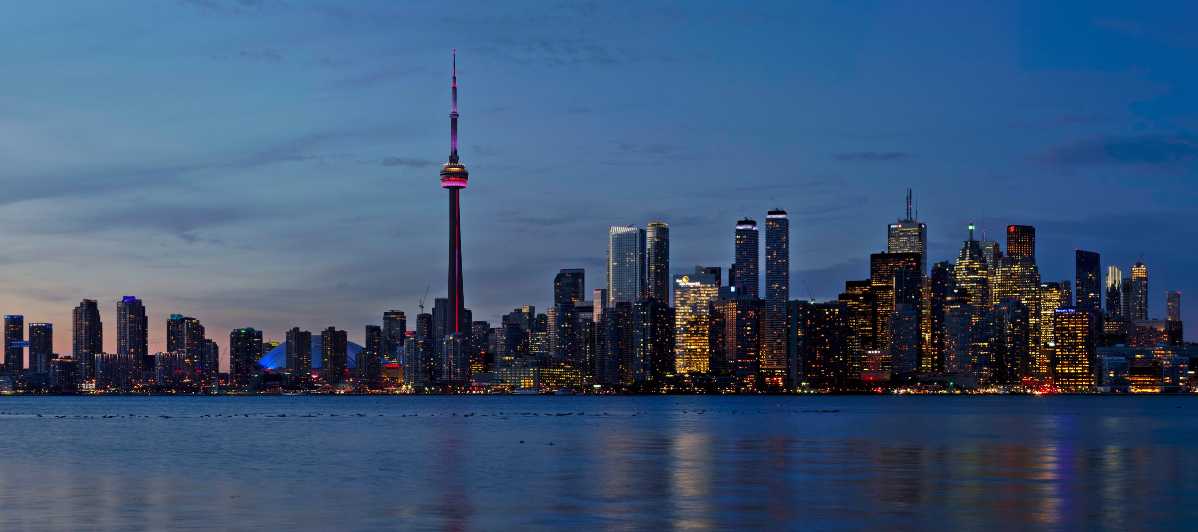 Toronto's illuminated downtown skyline and CN Tower across Lake Ontario at sunset