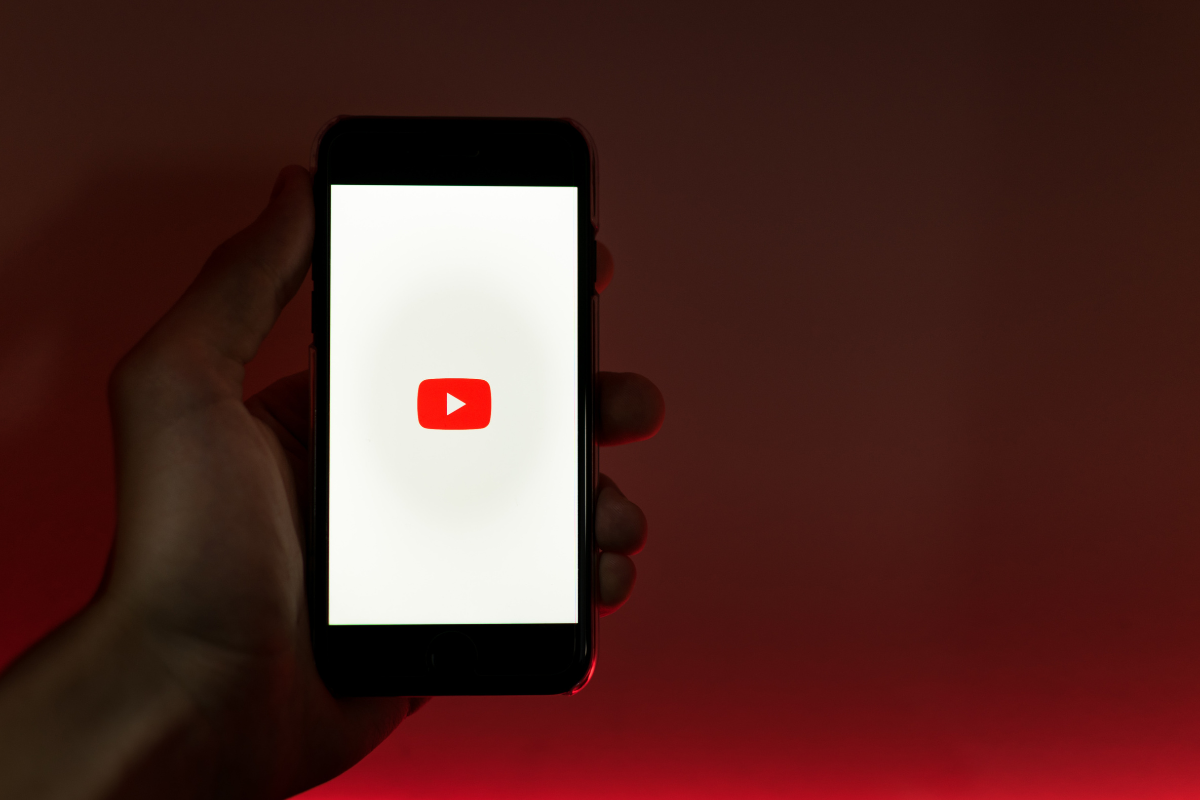 The photo shows a hand holding a mobile phone with YouTube turned on.