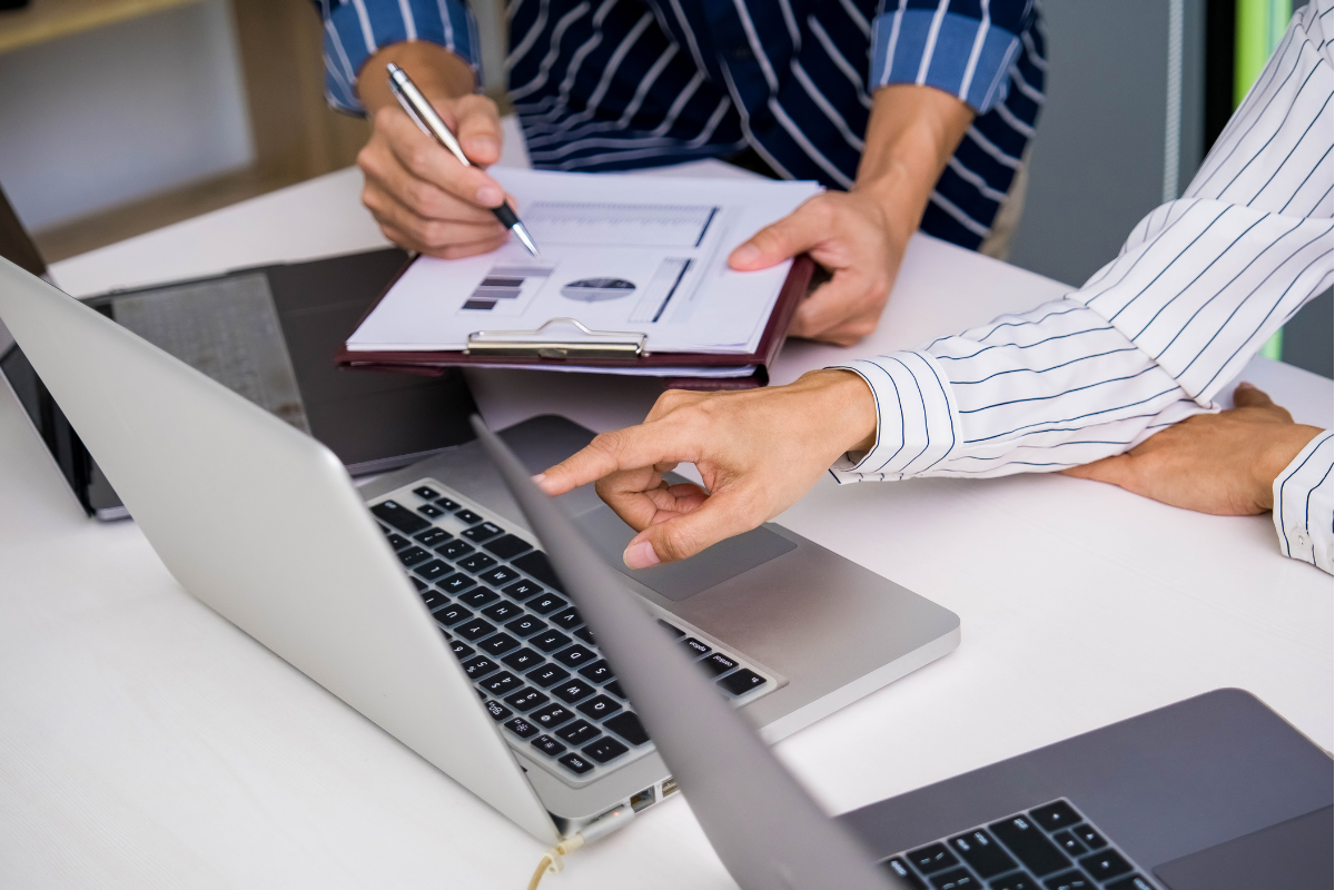 The image shows two people with papers and laptops working on a company analysis.