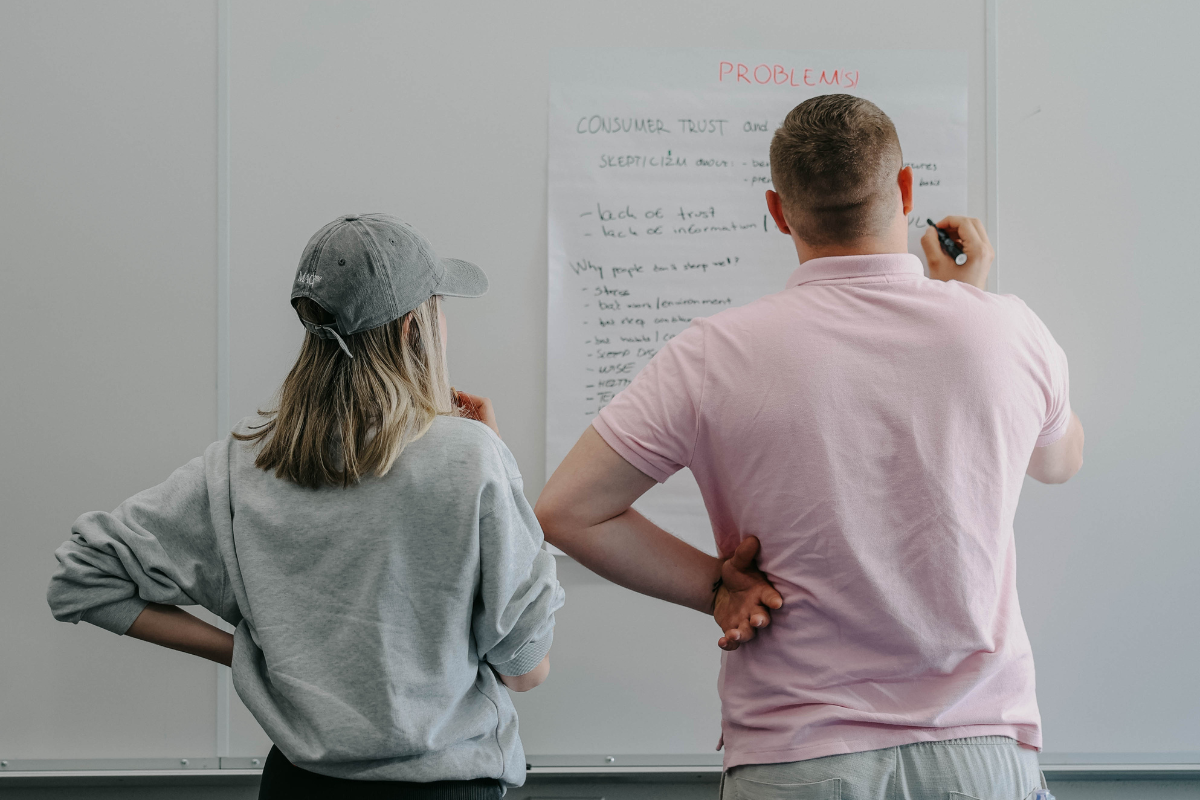 The image shows two participants at ABC Silicon Valley 2024 solving a task in front of a whiteboard.